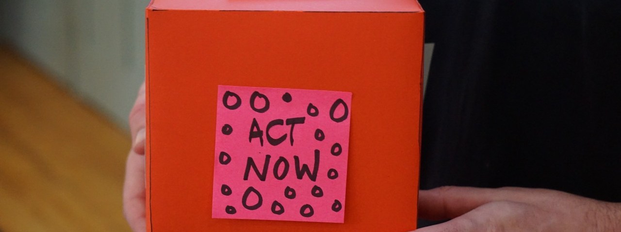 red donation box with a pick sticky note that says act now