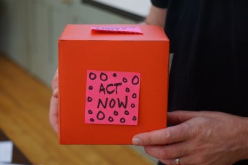 red donation box with a pick sticky note that says act now